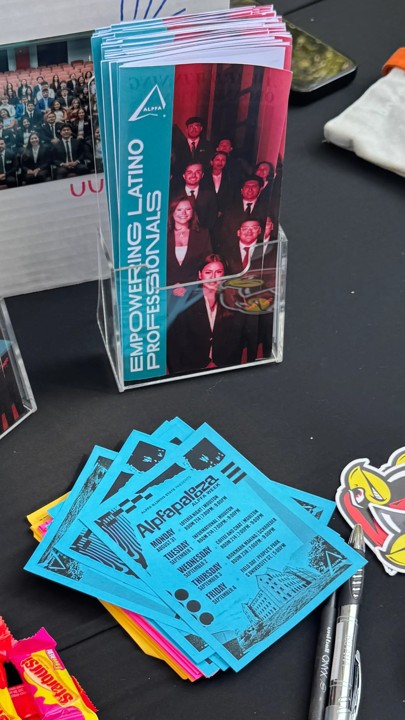 An ALPFA recruitment table with stacks of Empowering Latino Professionals brochures, blue Alpfapalooza flyers, ALPFA stickers and candy
