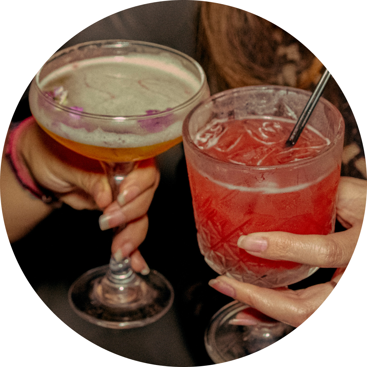 rounded photo of two different colorful drink being hold by a different hand