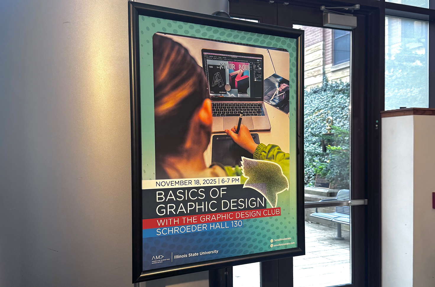 A photo of a poster displaying an event for 'Basics of Graphic Design', with information of the event and a photo of a girl drawing with her stylus to use her laptop.