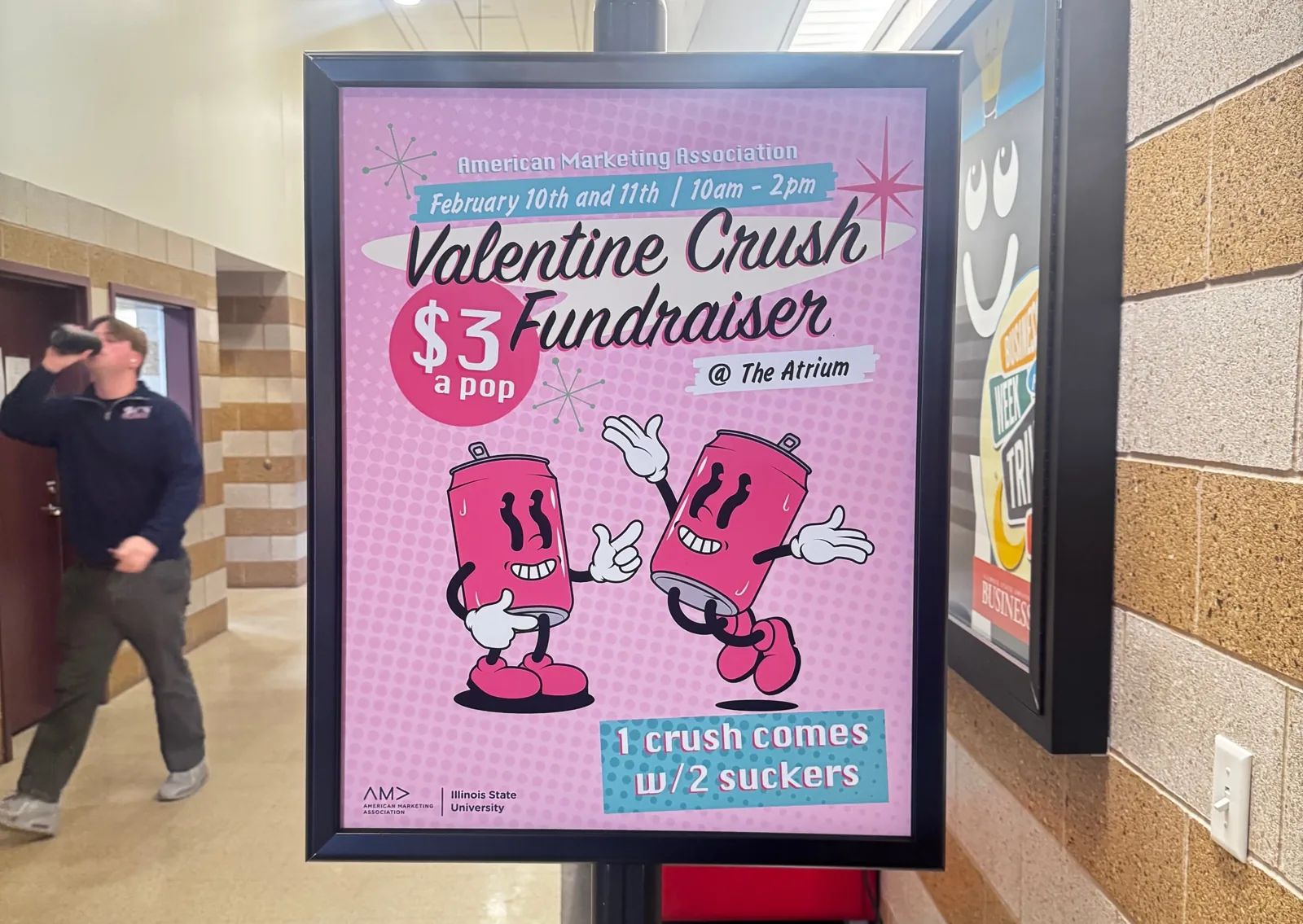 Pink Valentine Crush Fundraiser poster in a hallway display frame: retro script title, a $3 a pop badge, two smiling cartoon Crush soda cans, and the note that one Crush comes with two suckers, February 10 and 11 at the Atrium